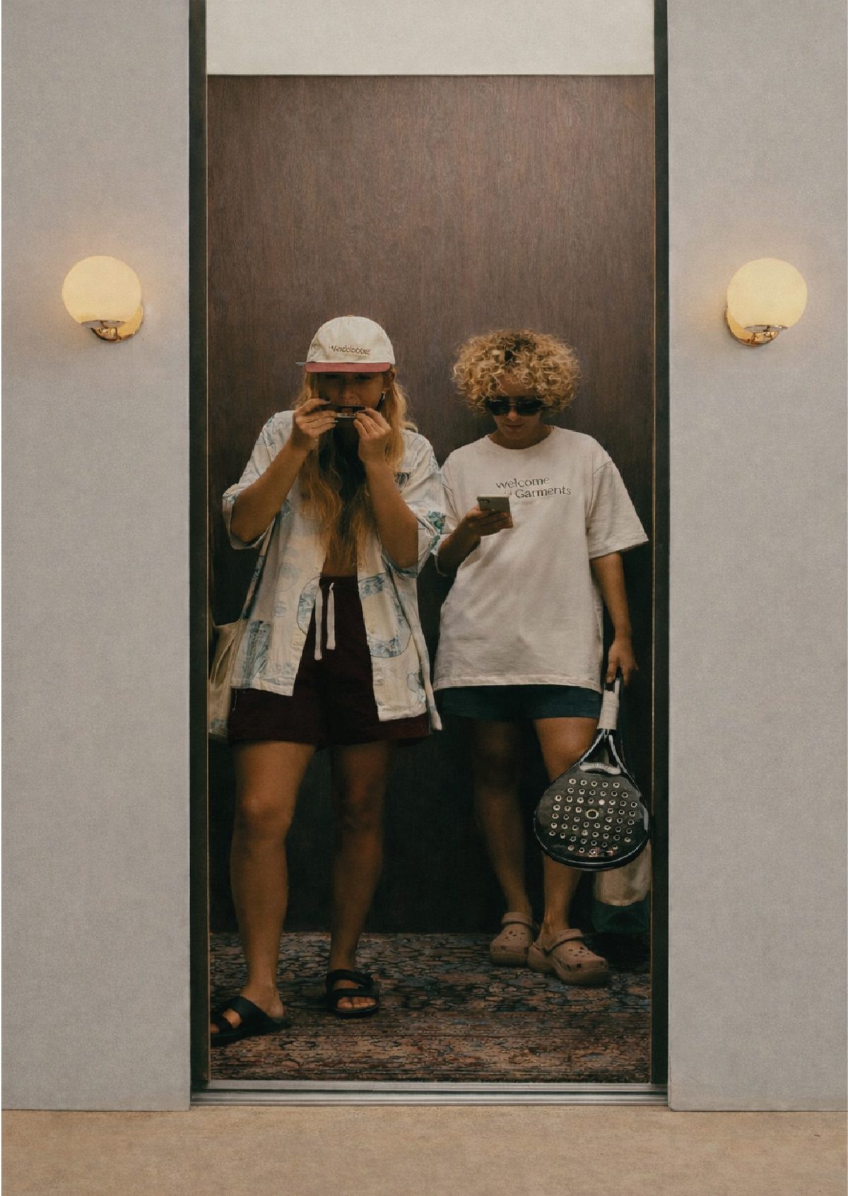 Dos amigas en un ascensor, una con una pala LION en la mano